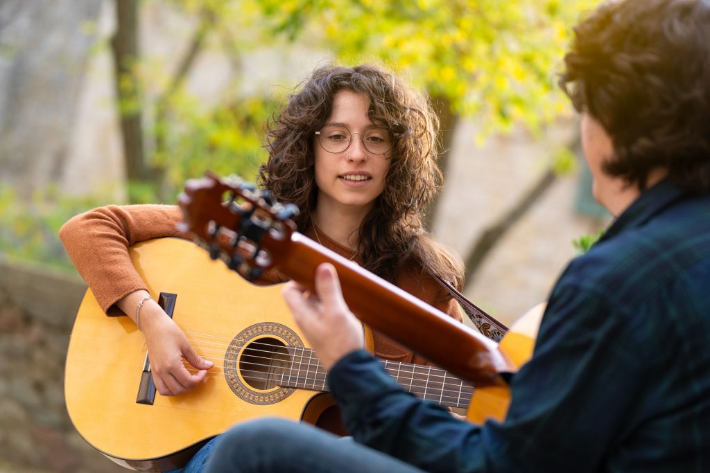 Brunette young girl learning to play Spanish guitar in the street with a teacher.